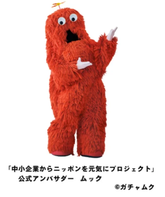 人気キャラクターのムックが、白い背景の前で両手を広げて立っている。これは「中小企業からニッポンを元気にプロジェクト」の公式アンバサダーとしての姿で、親しみやすいポーズをとっている。