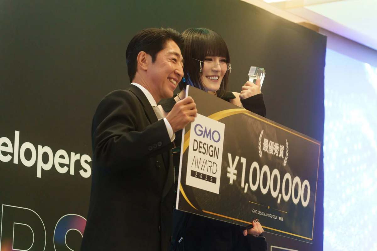 「GMO DESIGN AWARD 2025」の授賞式で、最優秀賞と賞金100万円のボード、そしてトロフィーを笑顔で受け取る二人の男女の様子を捉えた画像