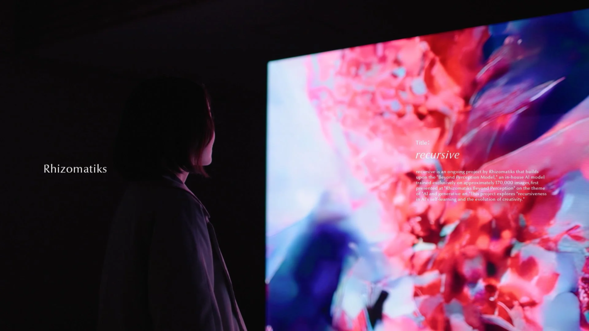 暗い空間で、一人の人物が鮮やかな色彩の抽象的なデジタルアートが映し出された大きなスクリーンを見つめている様子