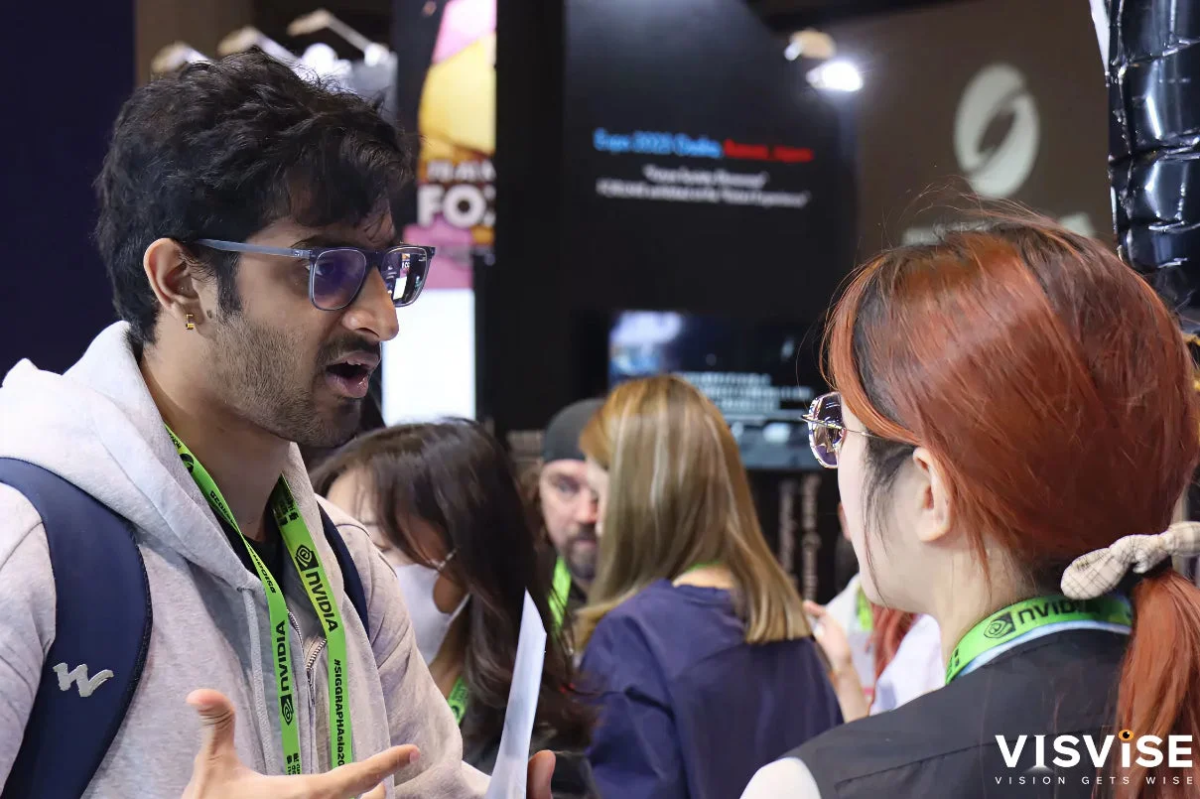 NVIDIAのストラップを着用した男性と女性が、展示会のような場所で会話している様子