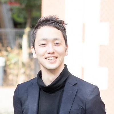 黒いタートルネックと紺色のジャケットを着た若いアジア人男性が、笑顔でカメラを見ているポートレート写真