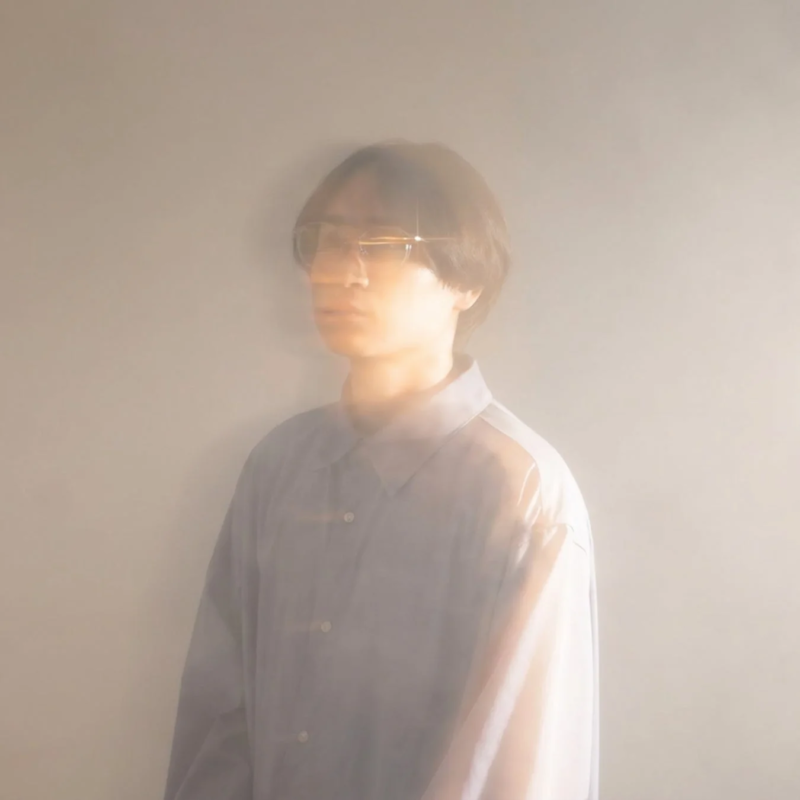 メガネをかけた人物が、ソフトフォーカスで幻想的な光の中に佇むポートレート