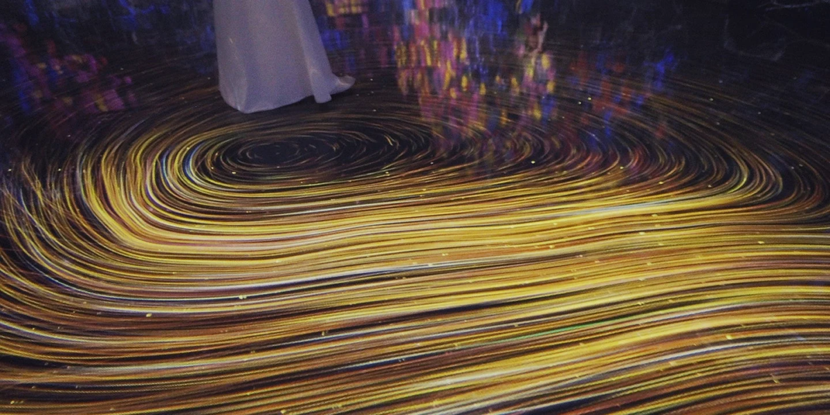 暗い空間の床に投影された渦巻くような金色の光のパターン