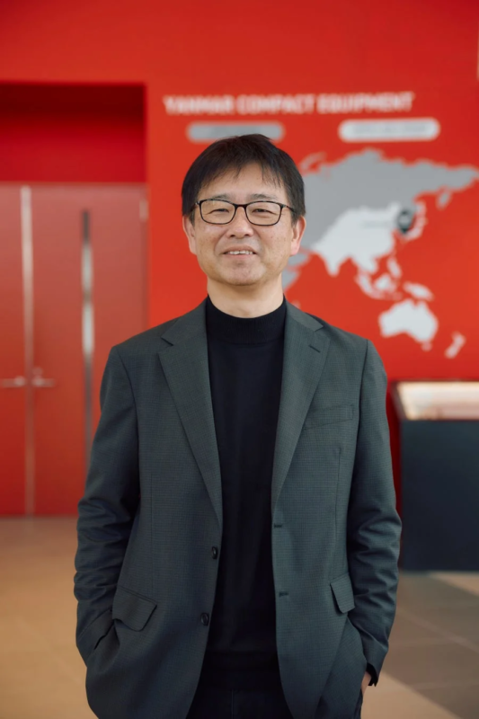 世界地図を背景に笑顔の田中氏