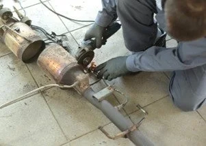 整備士がグラインダーを使って自動車の排気システムの一部を修理している様子