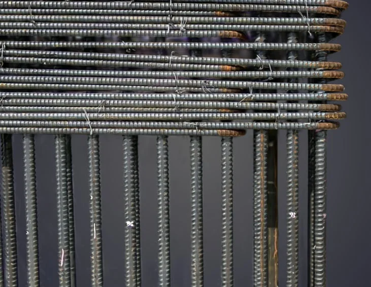 水平に何段も積み重ねられ、ワイヤーで固定された鉄筋と、垂直に並んだ鉄筋が写っています。