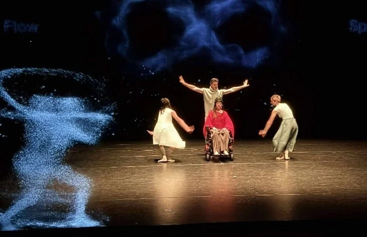 暗い舞台上で、車椅子のパフォーマーを含む4人がパフォーマンスを披露しています。