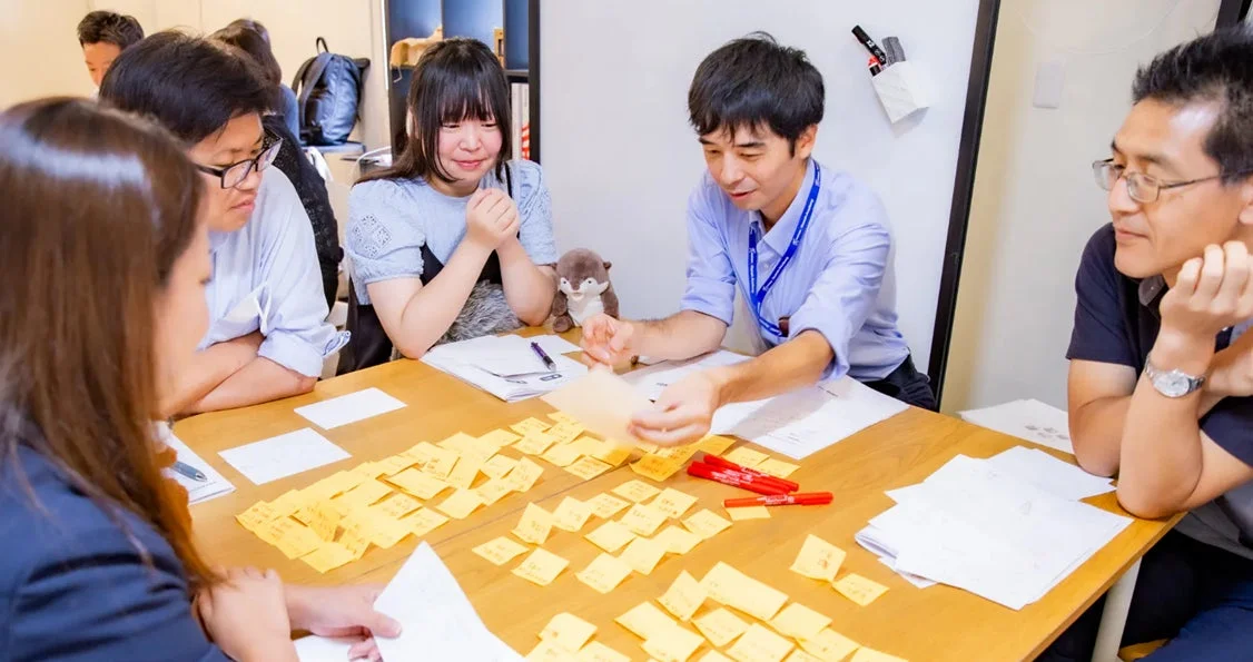 数人の人々がテーブルを囲み、ワークショップかブレインストーミングを行っている画像