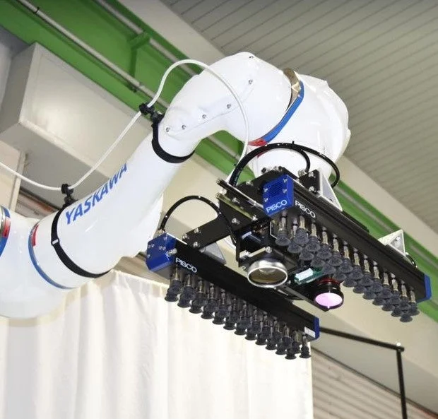 YASKAWA製の白い産業用ロボットアームが、PISCO製の多数の吸着パッドを備えたグリッパーとセンサーを装着している様子
