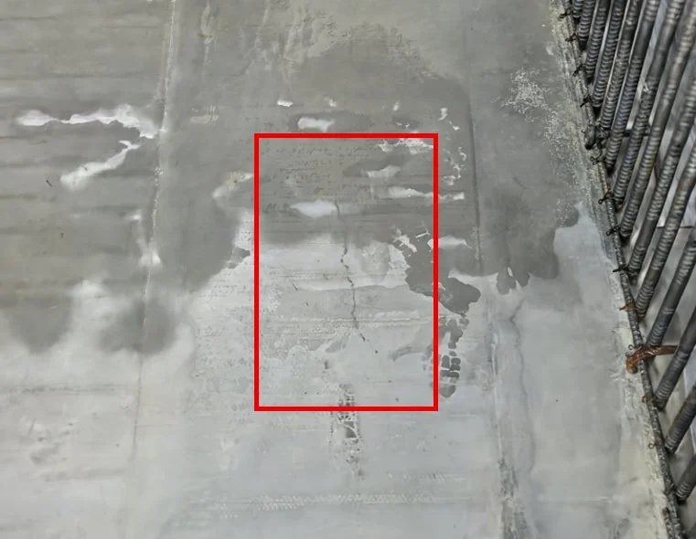 建設現場のコンクリート表面の画像。水濡れ跡やひび割れがあり、右側には鉄筋が見える。