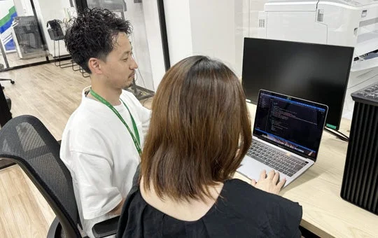 オフィスで男性と女性がノートパソコンを囲んで共同作業をしている様子