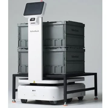 画面付きの白い自動搬送ロボットが、グレーの折りたたみコンテナを複数積んで移動している様子