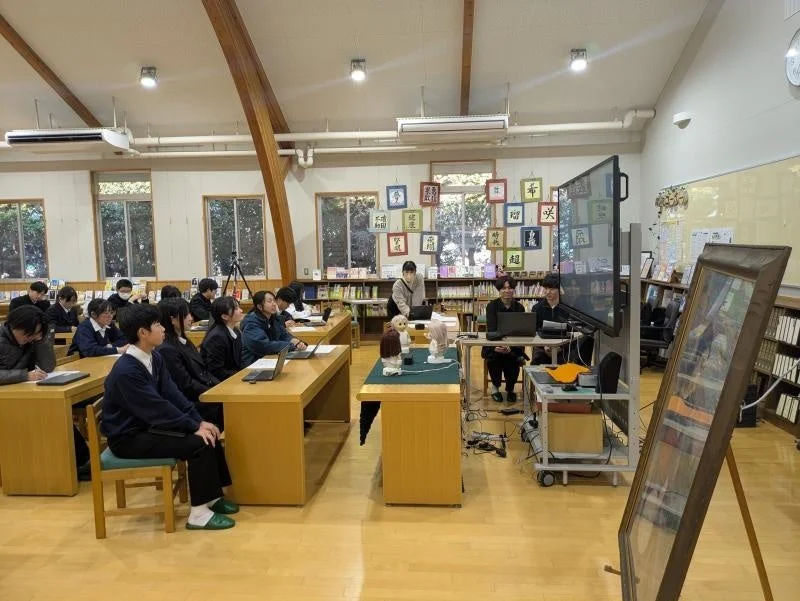 学校の図書館か多目的室で、生徒たちが授業やプレゼンテーションを受けている様子