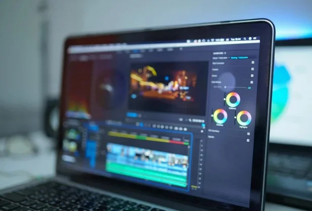ラップトップの画面に動画編集ソフトウェアのインターフェースが表示されています。カラー補正ツールやタイムラインが見え、映像制作やポストプロダクション作業中の様子がうかがえます。