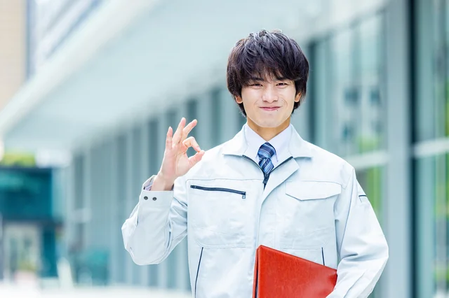 作業着姿の若い男性が笑顔でOKサインをしている