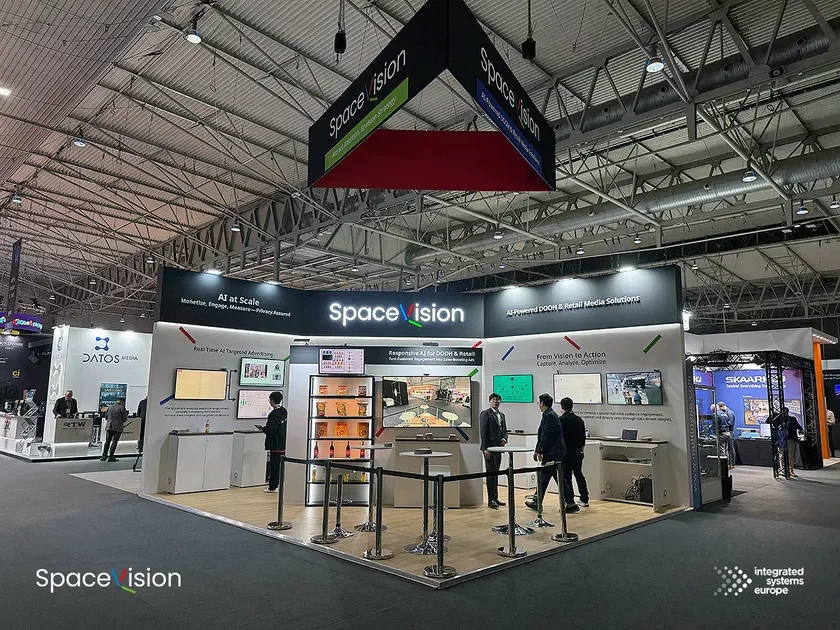 「Space vision」のモダンな展示ブースが写っており、AIを活用したDOOH(デジタル屋外広告)およびリテールメディアソリューションが紹介されています。複数のスクリーンがデータや広告を表示し、数人の参加者がブース内で技術に触れています。展示会「Integrated Systems Europe」で撮影されたもので、先進的なデジタル広告技術と小売テクノロジーに焦点が当てられている様子が伺えます。