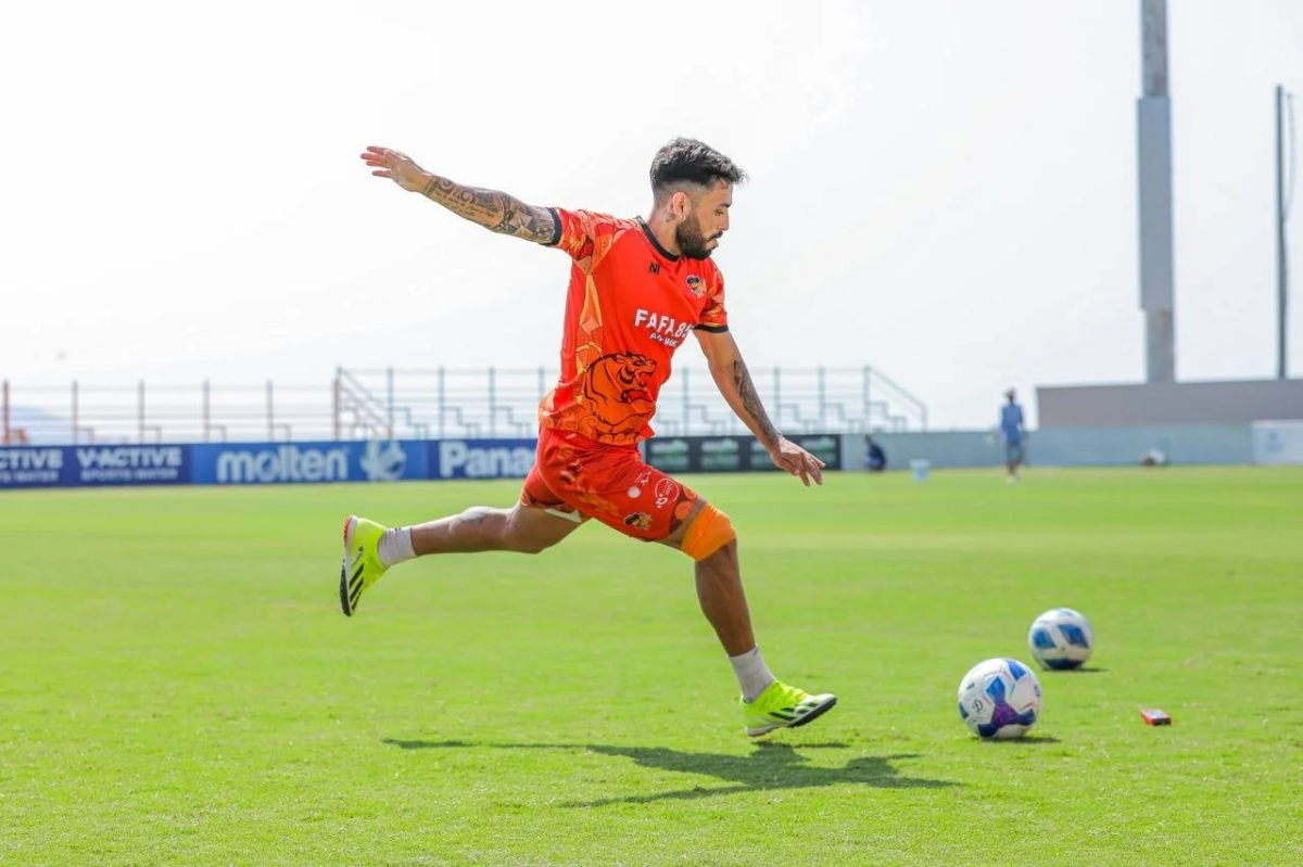 オレンジ色のユニフォームを着たサッカー選手がボールを蹴る瞬間