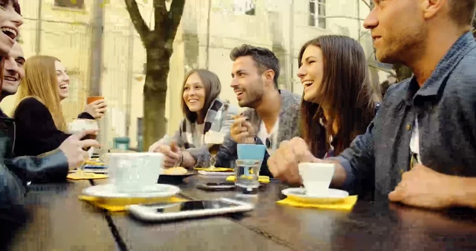 屋外のテーブルを囲んで座る若い男女のグループ