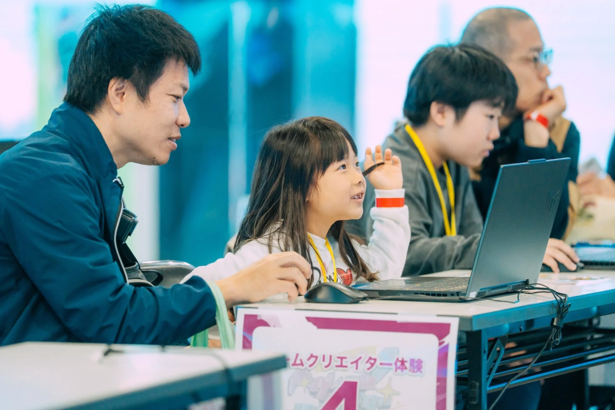 子供たちが大人と一緒にパソコンを操作しています