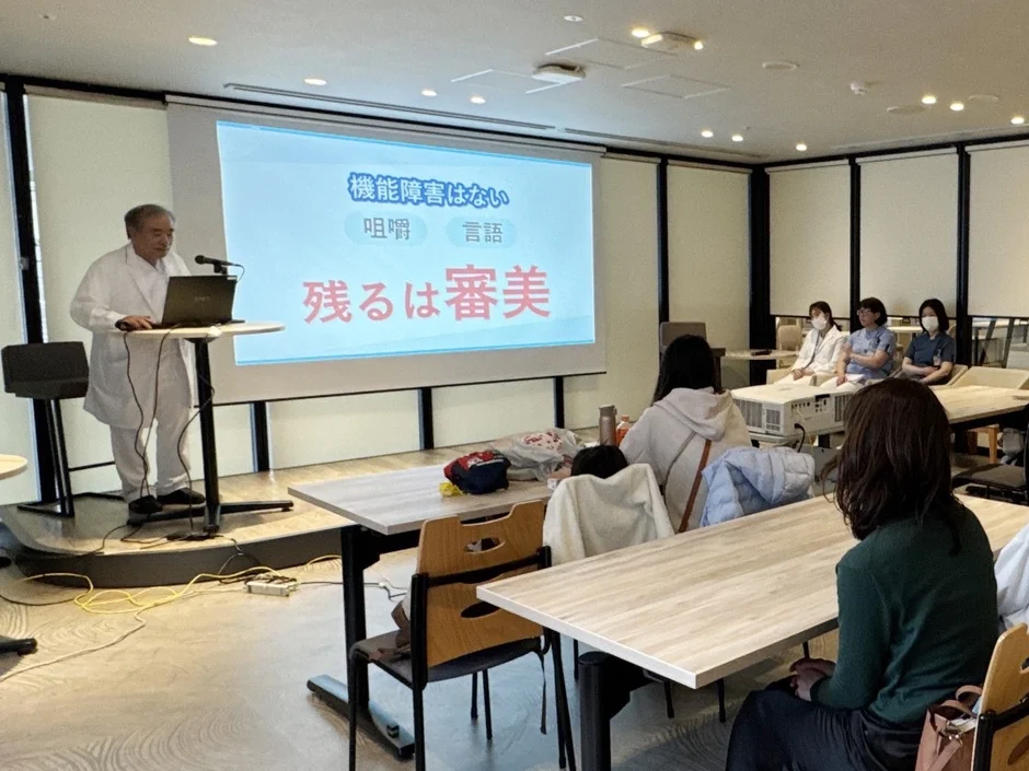 医療専門家による講演の様子。スクリーンには機能障害と審美に関する内容が表示されています。