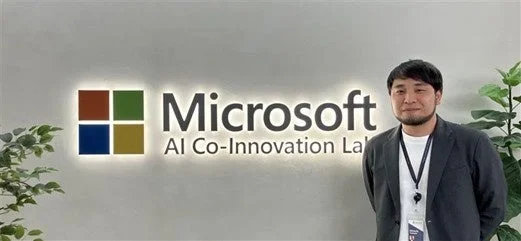 Microsoft AI Co-Innovation Labのロゴの前で、一人の男性が立っている様子を捉えた画像です。