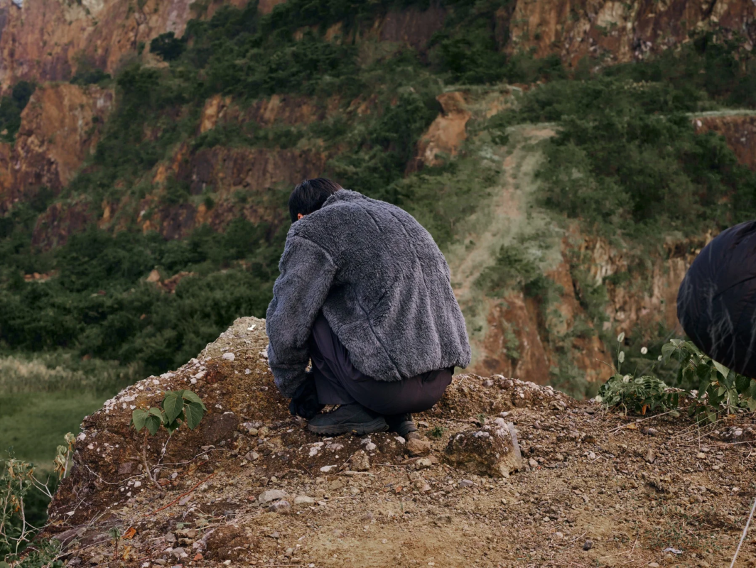岩場にしゃがみこむフリースジャケット着用者