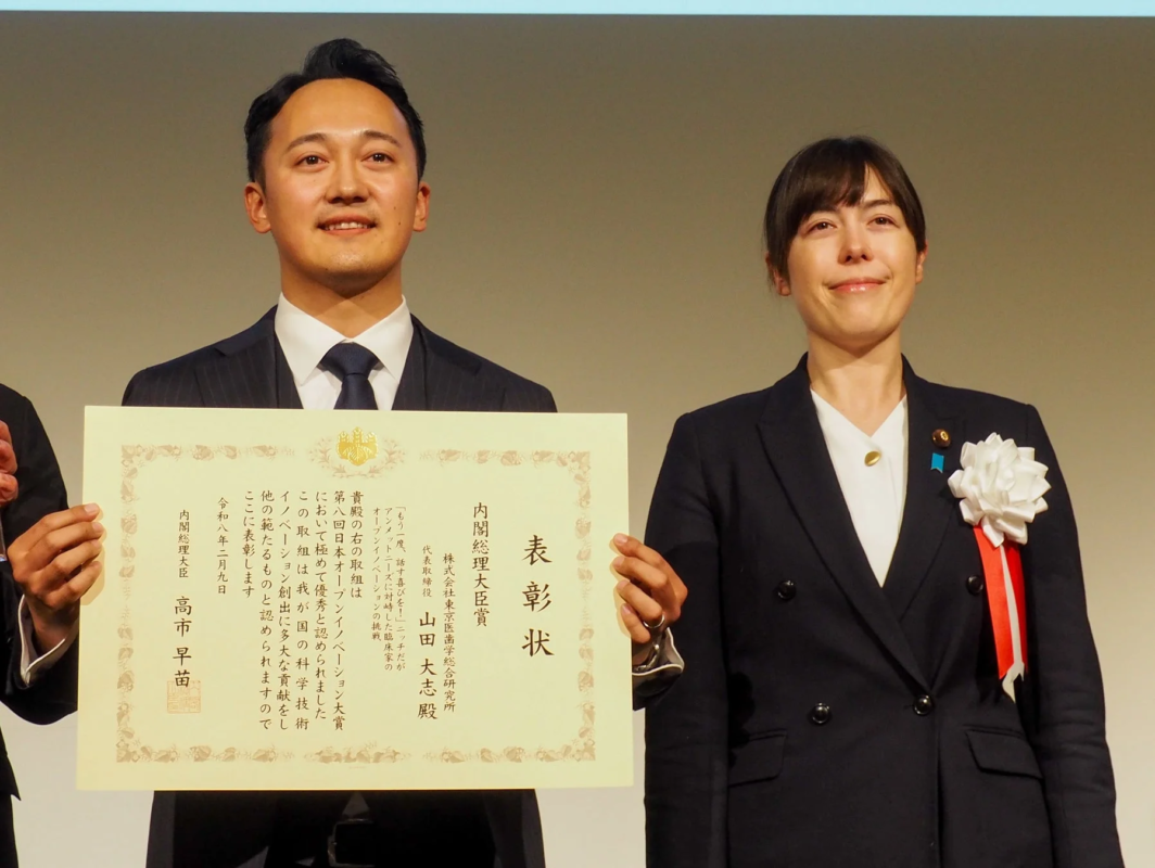 内閣総理大臣賞の表彰状を持つ山田社長と小野田大臣