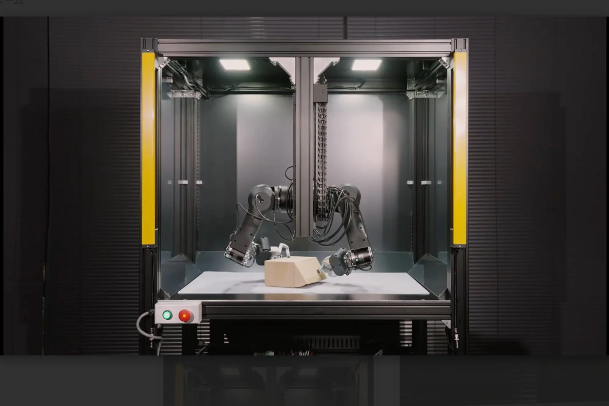 産業用のワークセル内で2本のロボットアームが箱を操作している様子