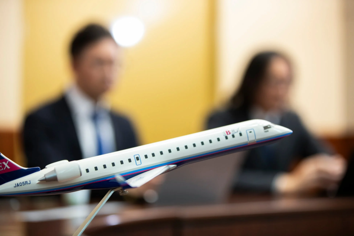 IBEXエアラインズの航空機模型がテーブルに置かれ、背景にはぼやけたビジネスパーソンが二人写っています。会議や商談の雰囲気を伝える一枚です。