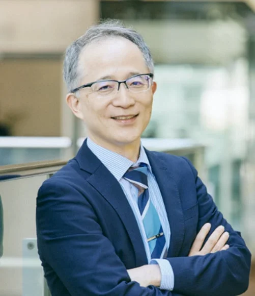 青いスーツとストライプのシャツ、ネクタイを着用し、眼鏡をかけたアジア系の男性