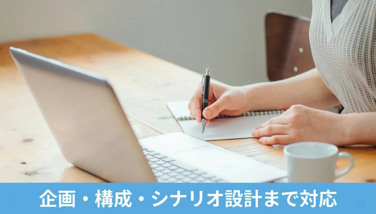 ノートパソコンを開き、ノートにペンで書き込んでいる人物の手元